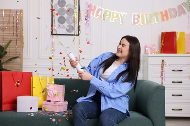 Photo of Happy woman blowing up confetti popper on sofa at home