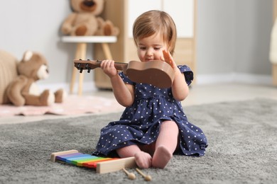 Photo of Cute little girl playing with toy guitar on floor at home