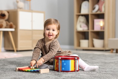 Cute little girl playing with toy xylophone on floor at home