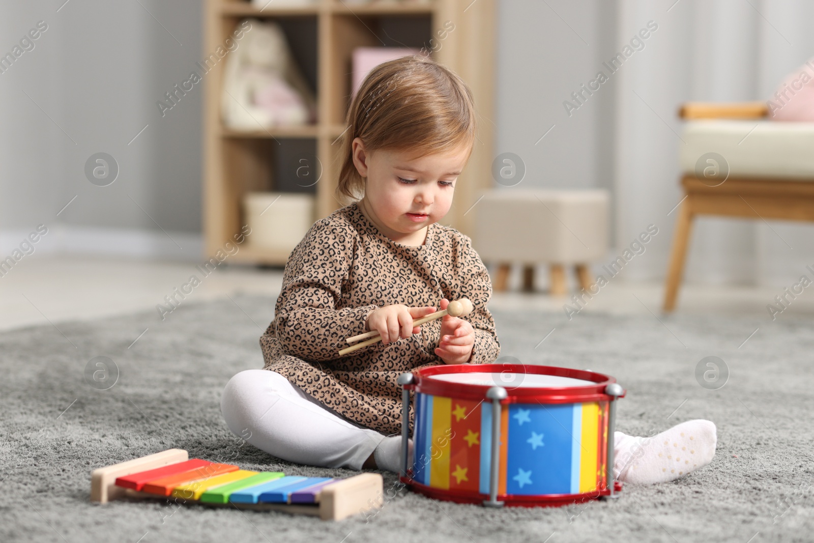 Photo of Cute little girl playing with toy musical instruments on floor at home