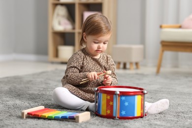 Photo of Cute little girl playing with toy musical instruments on floor at home