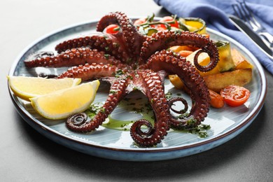 Fried octopus with herb sauce, lemon and vegetables on grey table, closeup