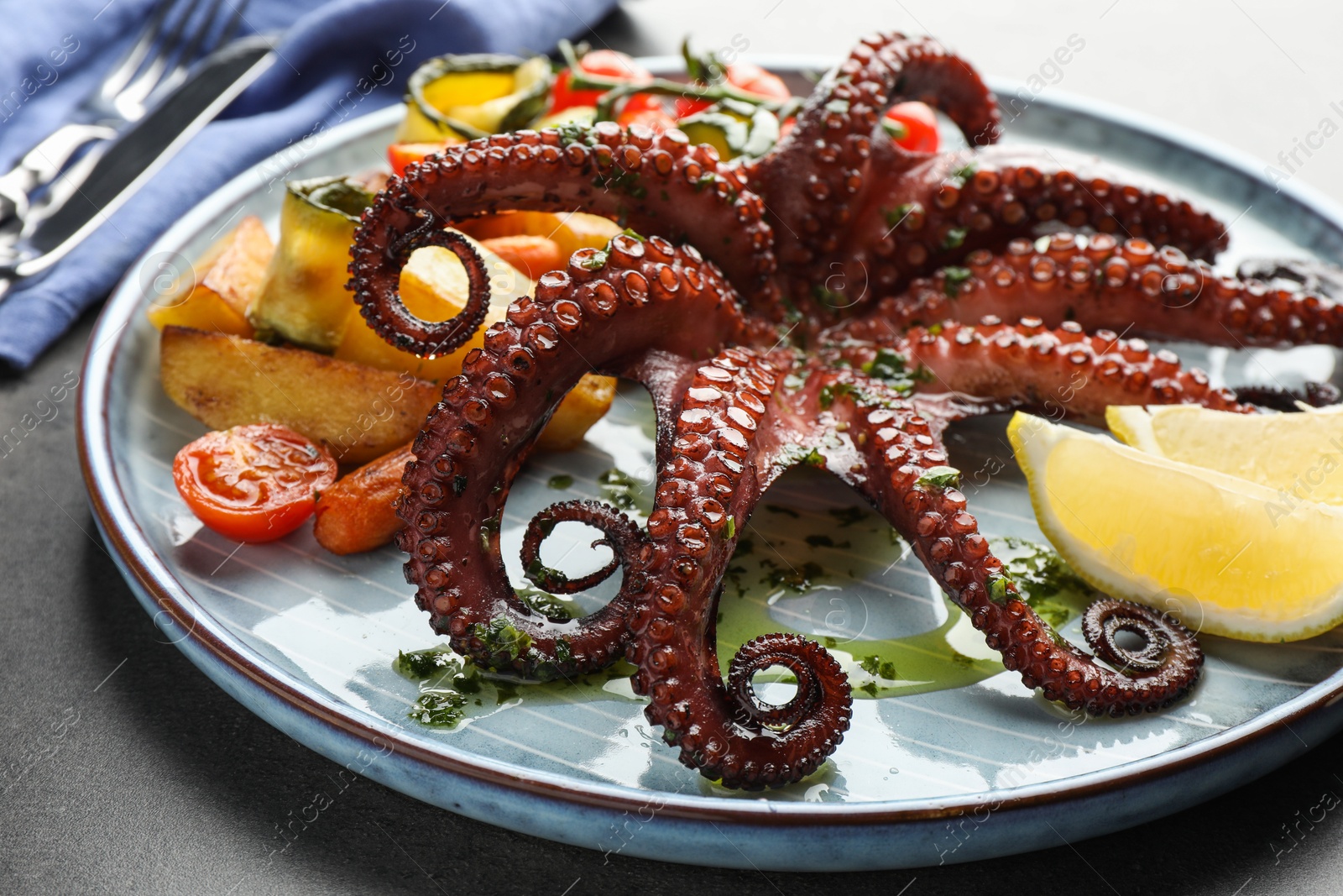 Photo of Fried octopus with herb sauce, lemon and vegetables on grey table, closeup