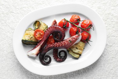 Photo of Fried octopus with zucchini and tomatoes on light textured table, top view