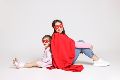 Mother and her cute little daughter wearing superhero costumes on white background