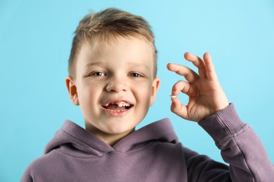 Photo of Cute little boy with missing tooth on light blue background. Waiting for tooth fairy