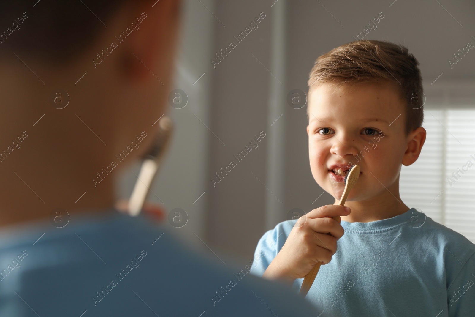 Photo of Cute little boy with missing tooth brushing his teeth near mirror indoors