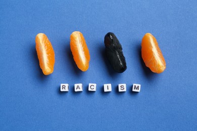 Photo of Word Racism and tangerine segments of different colors on blue background, flat lay