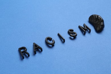 Photo of Word Racism and black tangerine segment on blue background, closeup