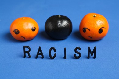 Photo of One black tangerine among orange ones and word Racism made with beads on blue background, closeup