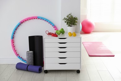 Photo of Different fitness equipment and chest of drawers indoors