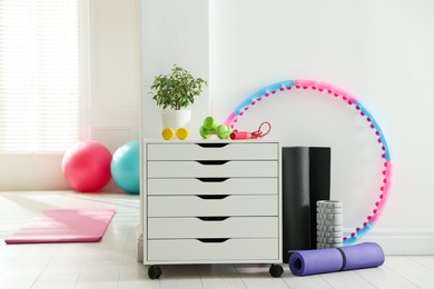 Photo of Different fitness equipment and chest of drawers indoors