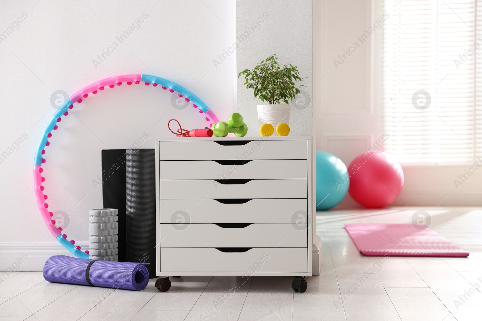 Photo of Different fitness equipment and chest of drawers indoors