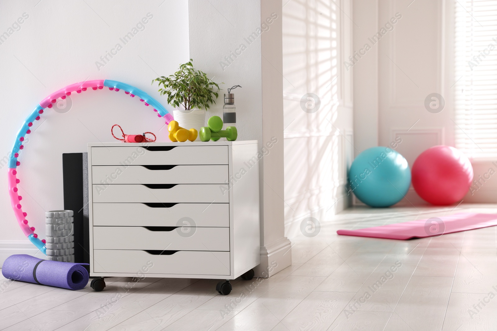 Photo of Different fitness equipment and chest of drawers indoors