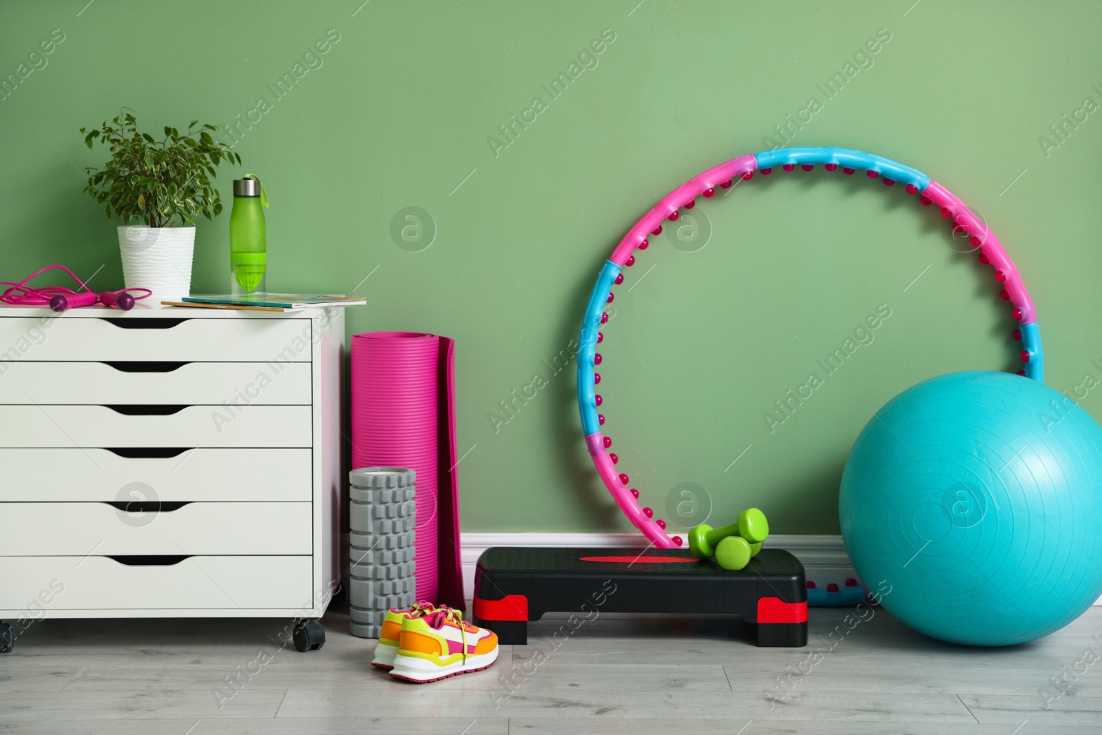 Photo of Different fitness equipment, sneakers and chest of drawers near green wall indoors