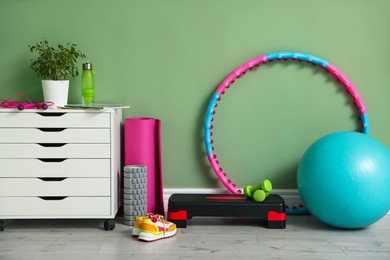 Different fitness equipment, sneakers and chest of drawers near green wall indoors