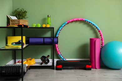 Different fitness equipment and sneakers near green wall indoors