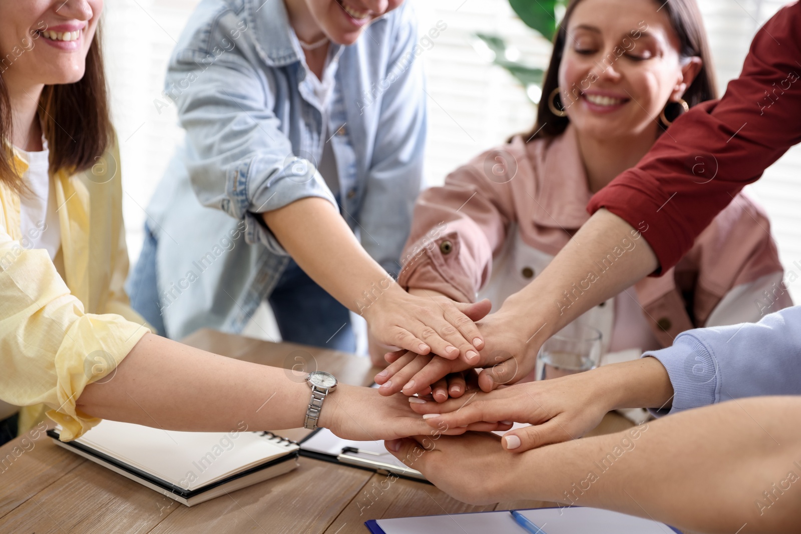 Photo of Unity concept. People holding hands together at wooden table indoors, closeup