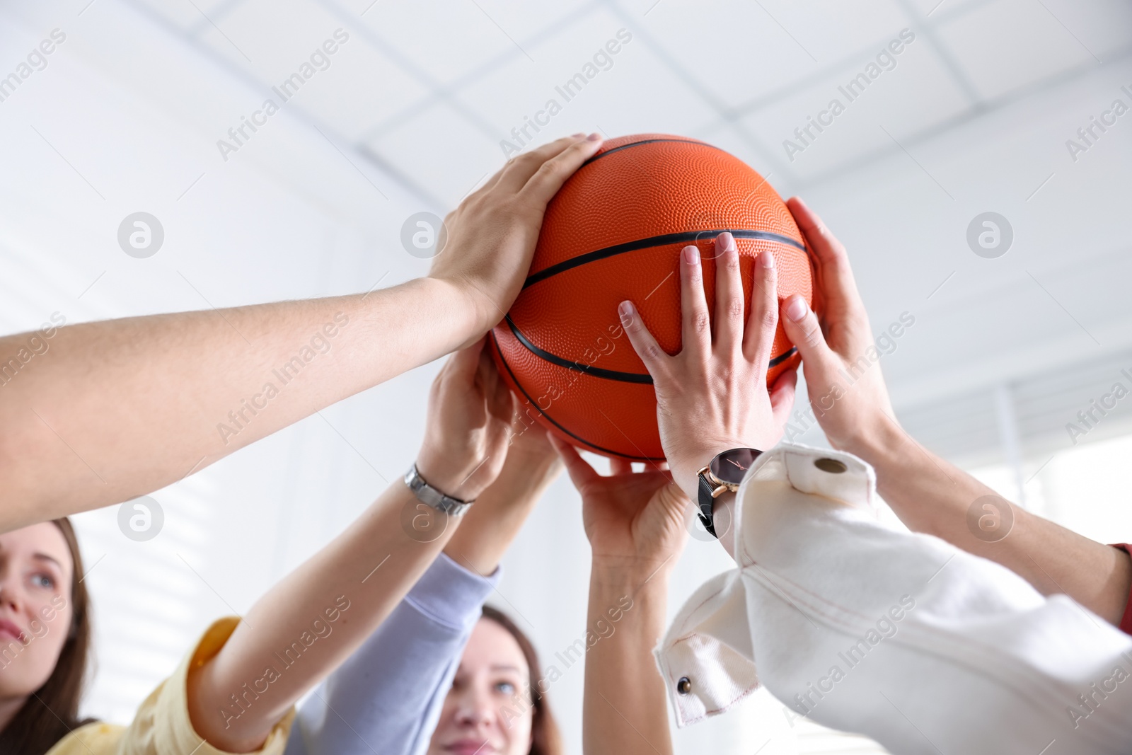 Photo of Unity concept. People holding basketball ball together indoors, low angle view