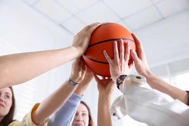 Unity concept. People holding basketball ball together indoors, low angle view