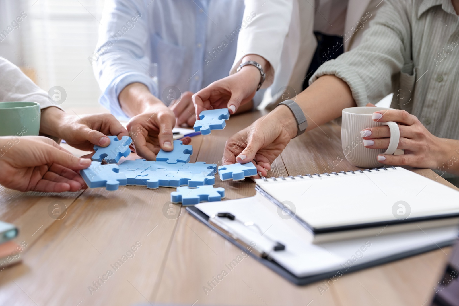 Photo of Unity concept. People putting puzzle pieces together at wooden table indoors, closeup