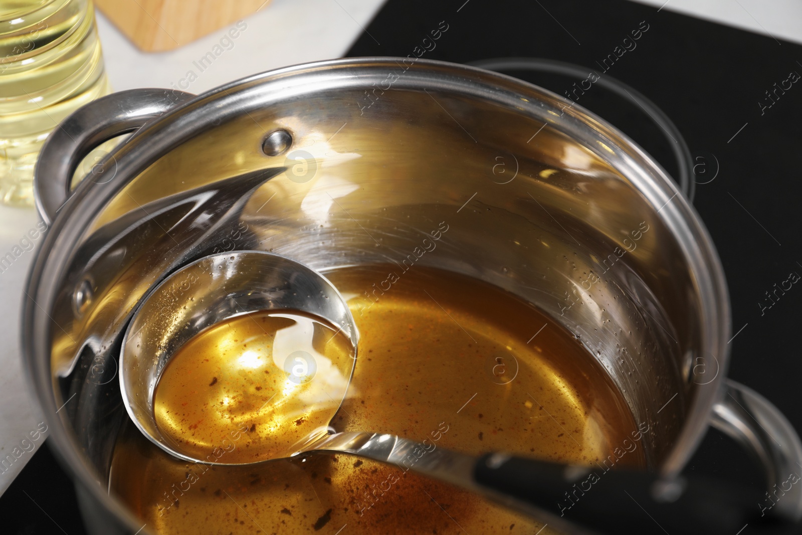 Photo of Used cooking oil and ladle in saucepan on stove, closeup