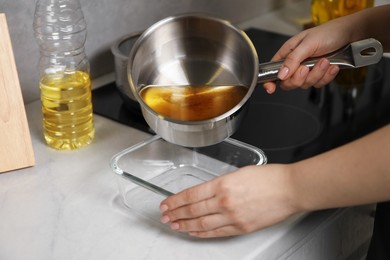 Photo of Woman pouring used cooking oil into glass container at white marble countertop, closeup