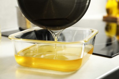 Photo of Pouring Used cooking oil into glass container at white countertop, closeup