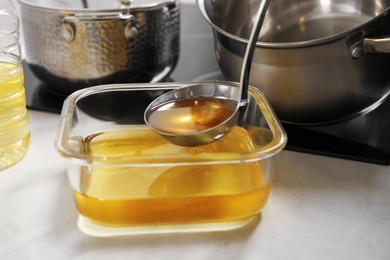 Photo of Pouring used cooking oil into glass container at white countertop, closeup