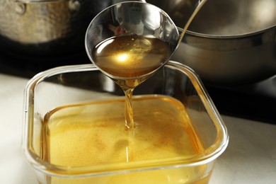 Photo of Pouring used cooking oil into glass container at white countertop, closeup