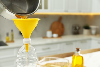 Photo of Pouring used cooking oil into bottle through funnel in kitchen, closeup. Space for text