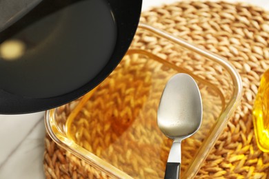 Photo of Pouring used cooking oil into glass container at white table, closeup