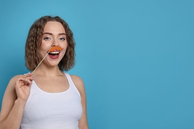 Photo of Happy woman with fake paper mustache on light blue background. Space for text