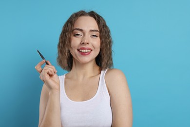 Photo of Smiling woman with tweezers on light blue background. Mustache removal tool