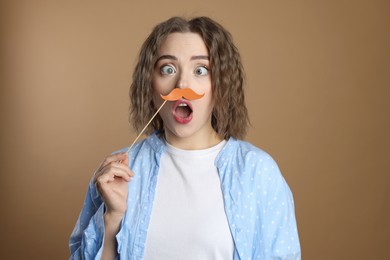 Funny woman with fake paper mustache on beige background