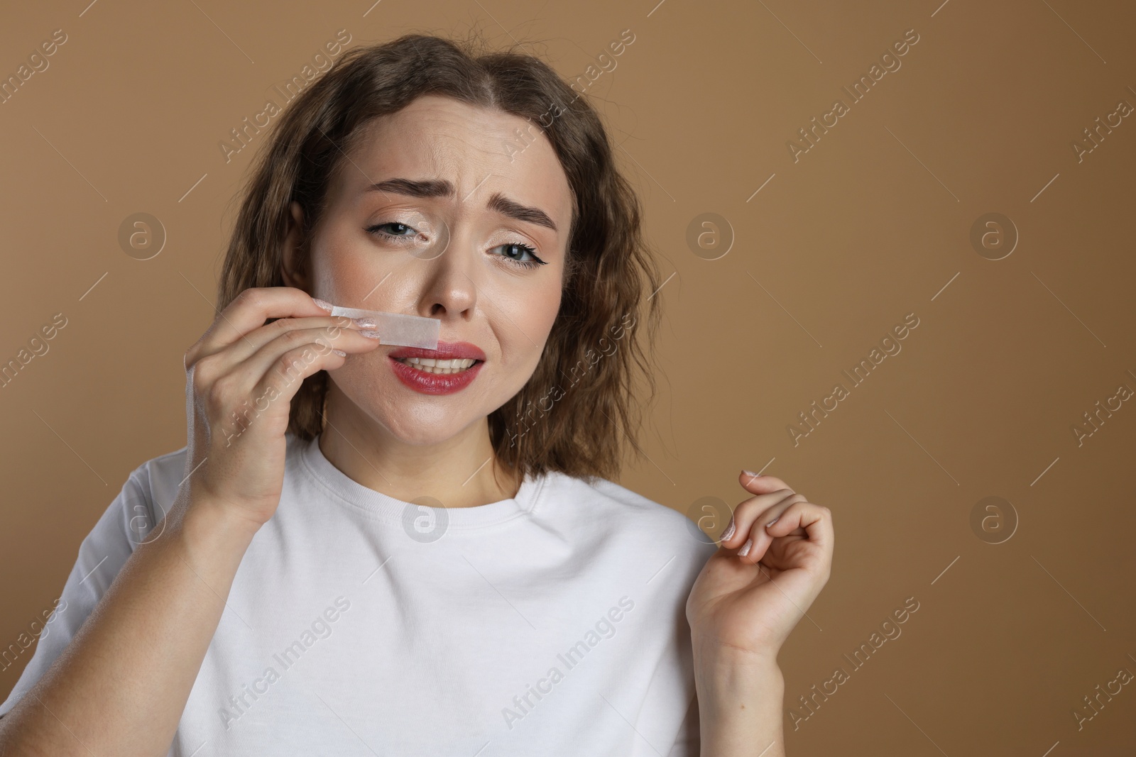 Photo of Emotional woman removing her mustache with wax strip on beige background. Space for text