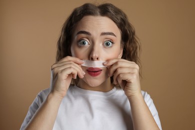 Photo of Emotional woman removing her mustache with wax strip on beige background