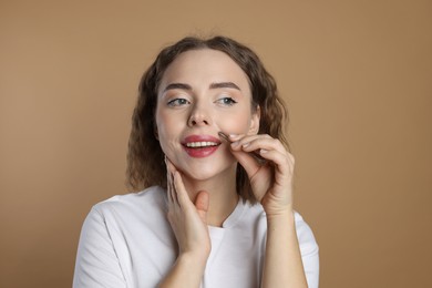 Photo of Happy woman plucking her mustache with tweezers on beige background