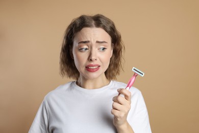 Emotional woman with razor on beige background. Hair removal tool