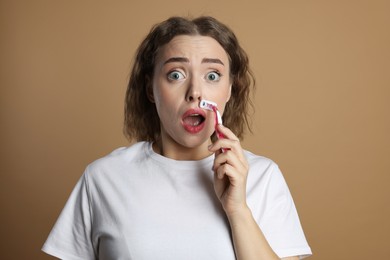 Photo of Emotional woman shaving her mustache with razor on beige background