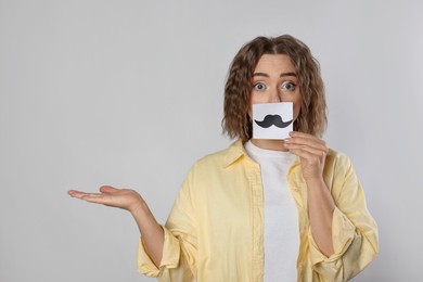 Photo of Woman holding paper with drawn mustache on grey background. Space for text