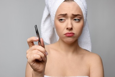 Photo of Beautiful woman with tweezers on grey background. Mustache removal tool