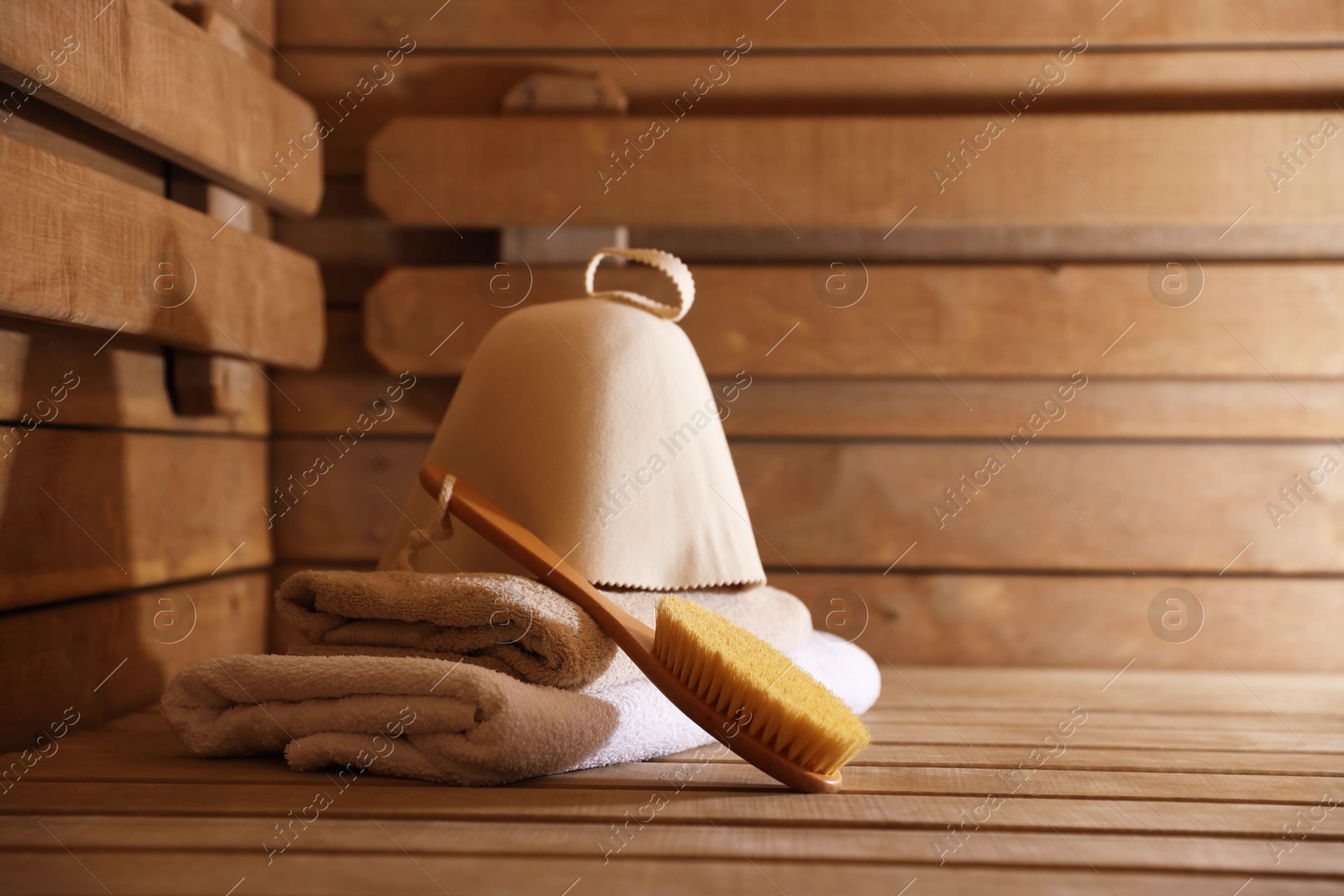 Photo of Massaging brush, hat and towels on wooden bench in sauna. Space for text