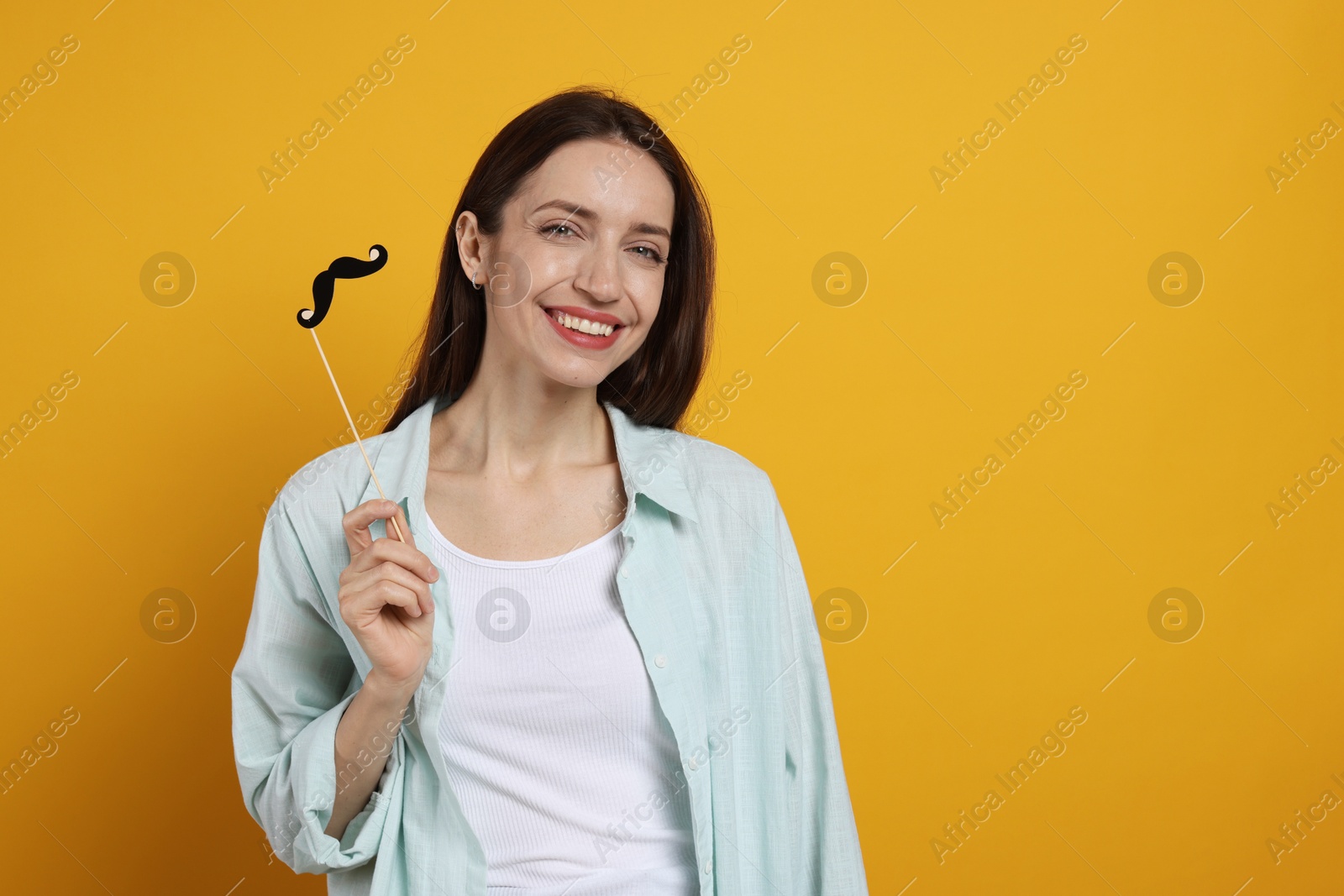 Photo of Happy woman with fake paper mustache on orange background. Space for text