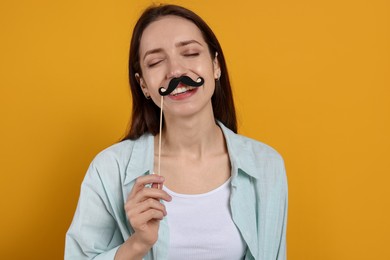 Photo of Happy woman with fake paper mustache on orange background