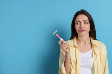 Photo of Beautiful woman with razor on light blue background, space for text. Hair removal tool