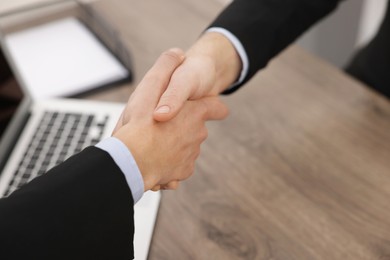 Businessmen shaking hands at wooden desk in office, closeup