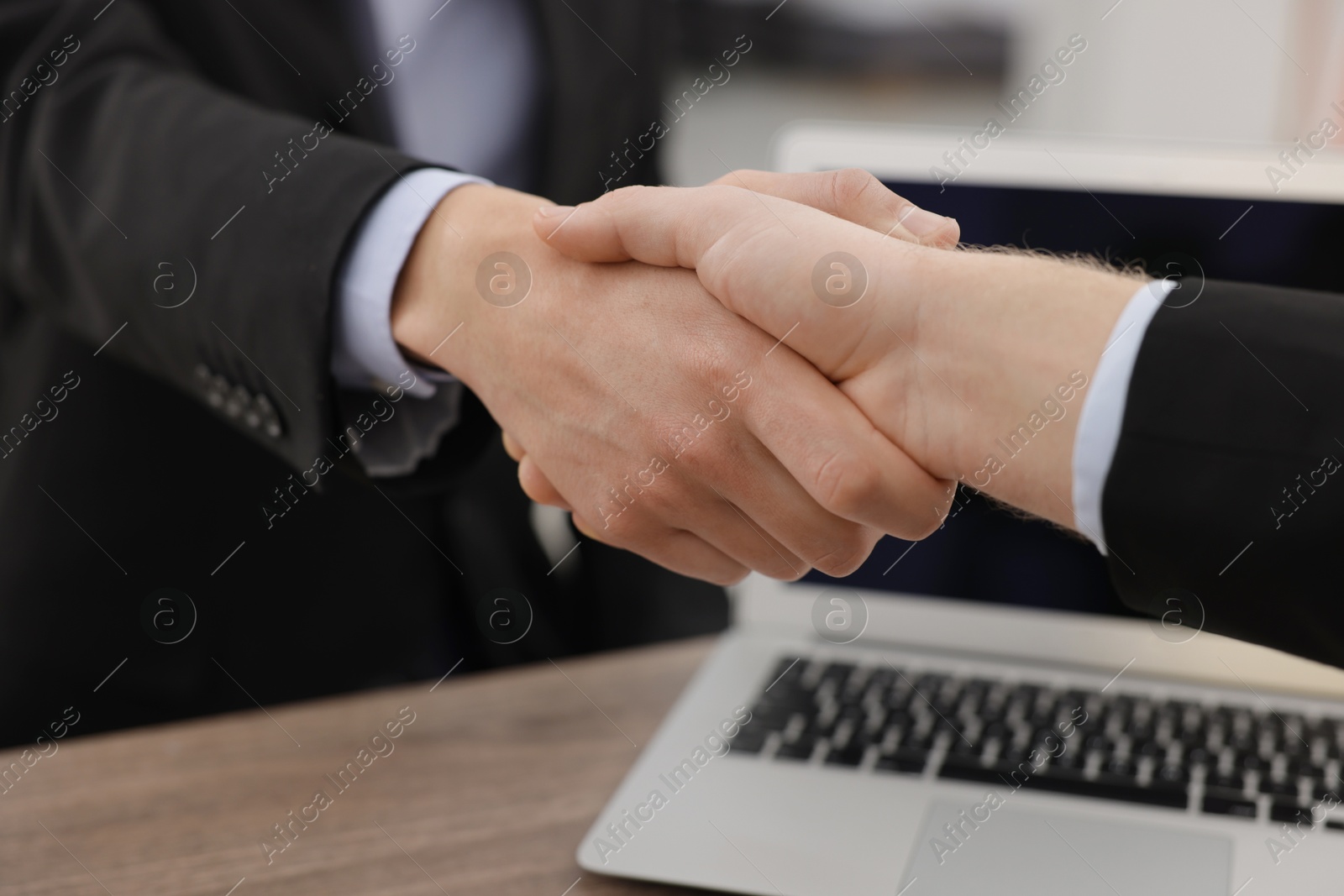 Photo of Businessmen shaking hands at wooden desk in office, closeup