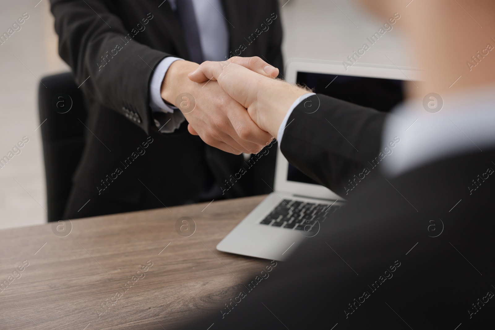 Photo of Businessmen shaking hands at wooden desk in office, closeup