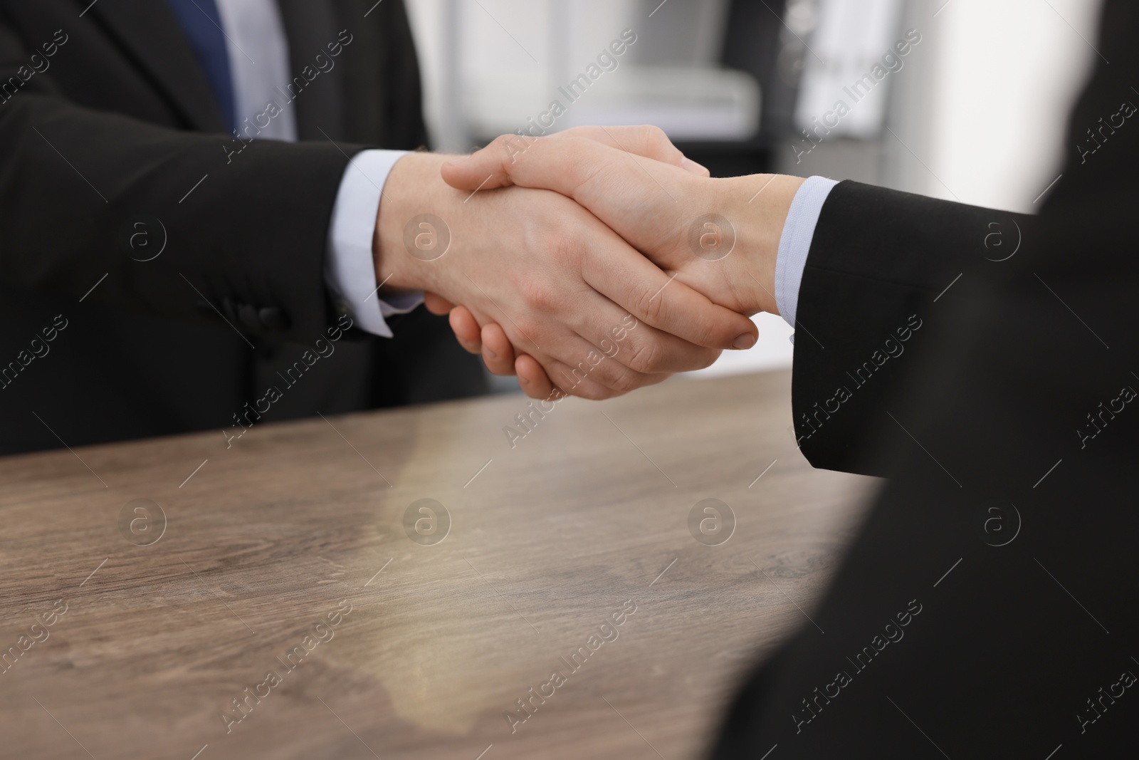 Photo of Businessmen shaking hands at wooden desk in office, closeup